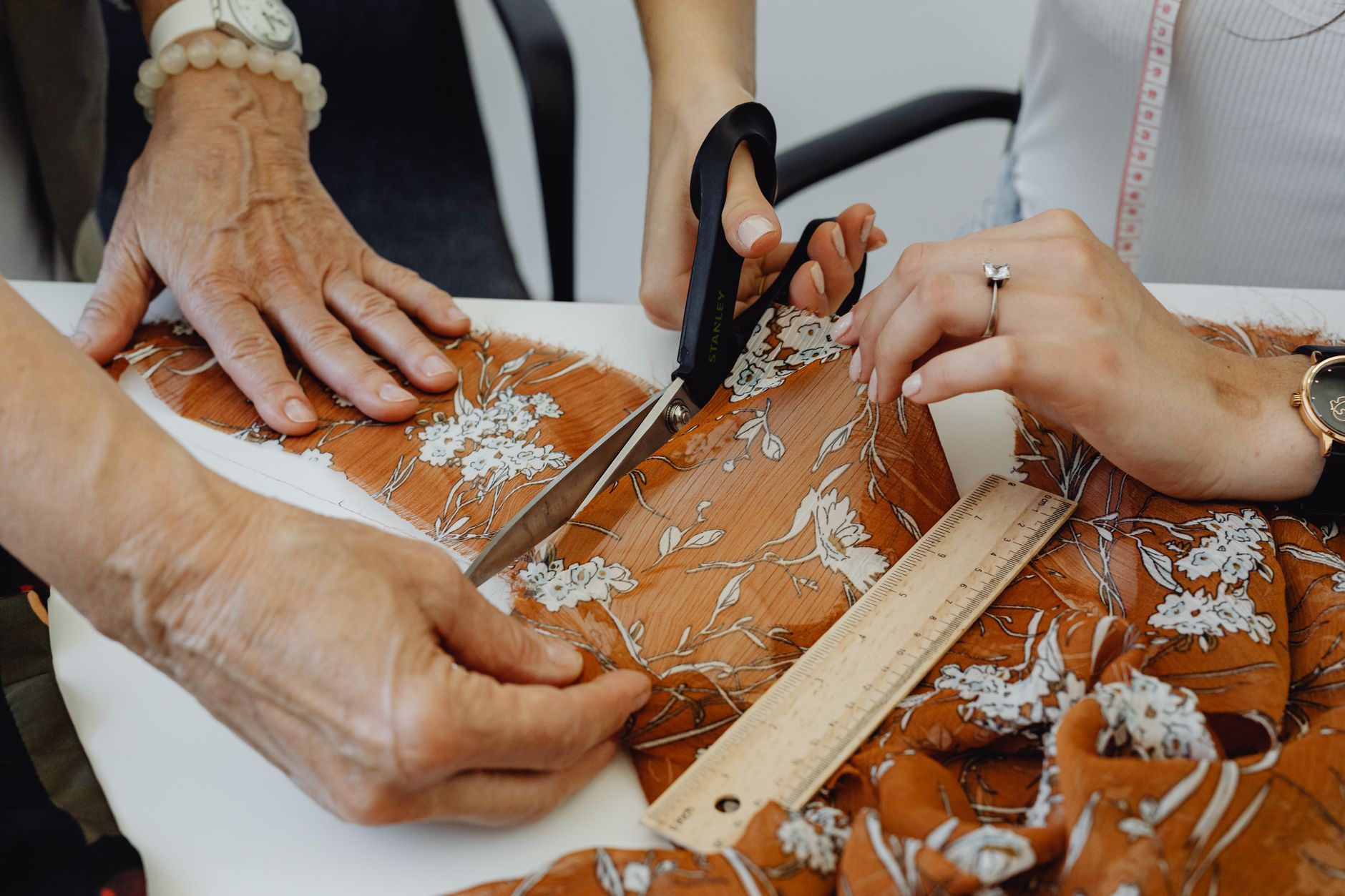 Two individuals cutting floral fabric with scissors in a tailoring workshop.