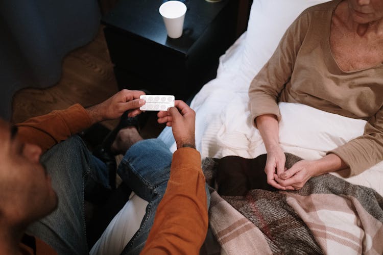 Man Giving Medicine To Elderly Woman In Bed