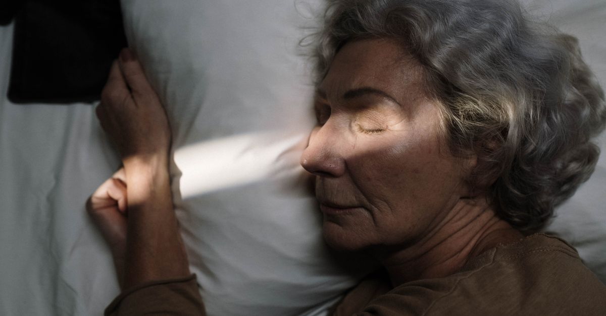 Serene image of elderly woman resting peacefully on pillow with sunlight grazing her face.