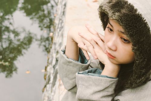 Free Thoughtful teenage girl wearing a warm coat, gazing by a pond, reflecting a serene mood. Stock Photo