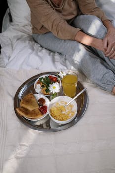 Cozy morning breakfast in bed with cereal, juice, and toast on a tray.