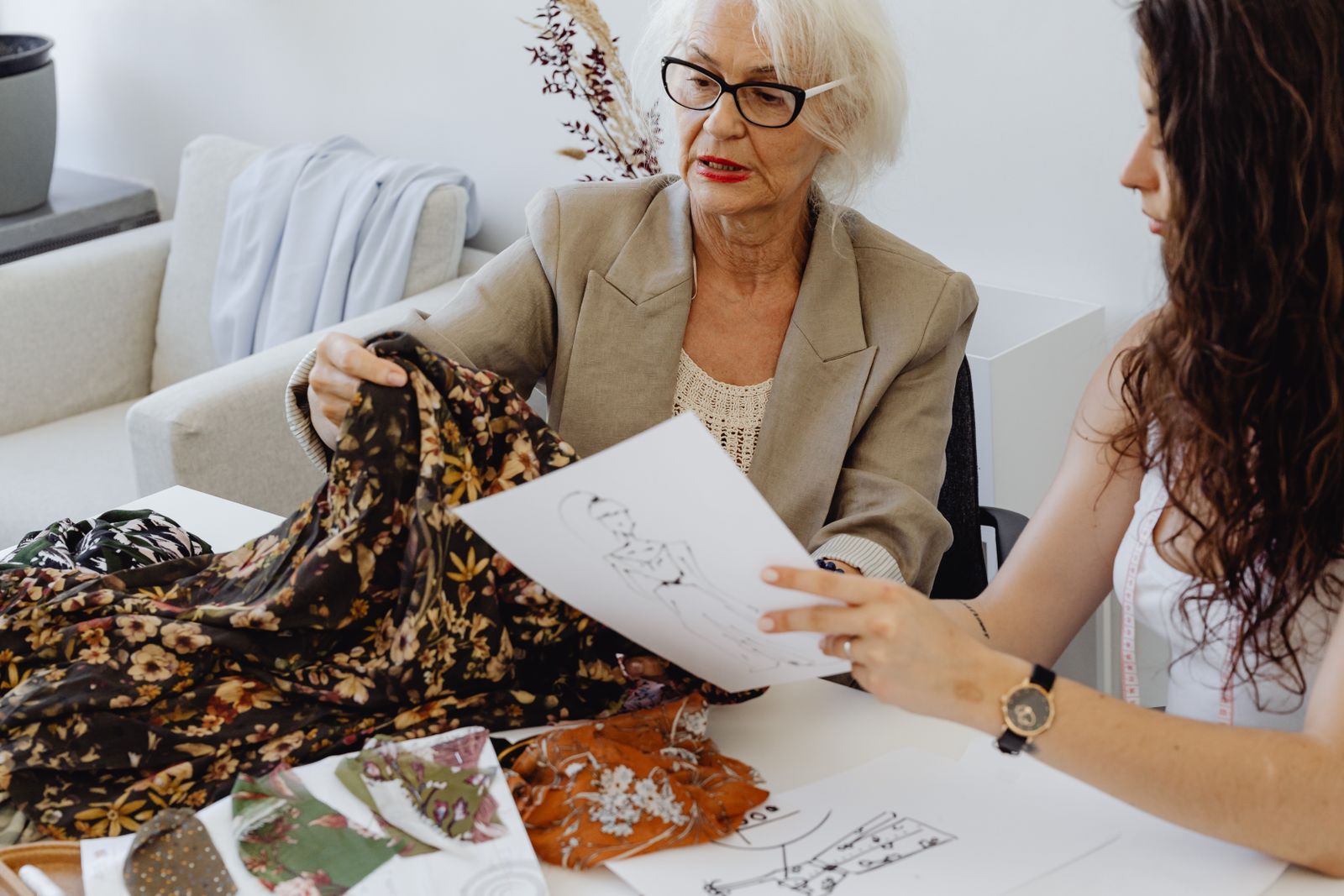 A senior designer and a colleague reviewing a printed fabric sample against sketches
