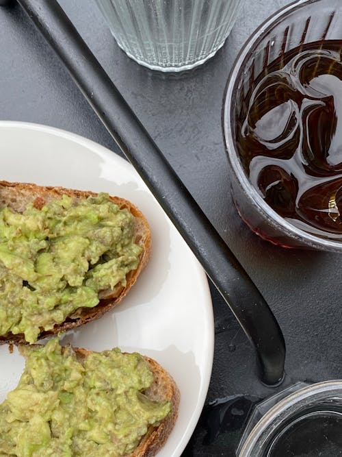 Free Breads with Avocado Spread on White Ceramic Plate Beside a Glass of Tea with Ice Stock Photo