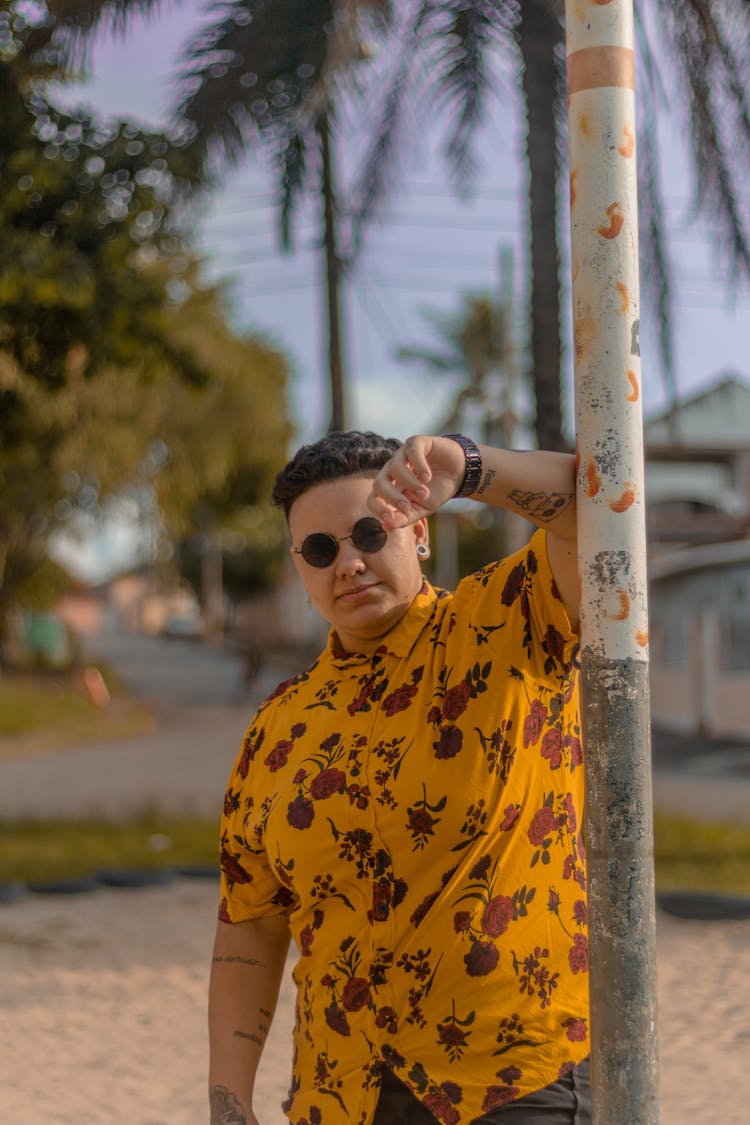 A Man In A Yellow Floral Print Shirt Leaning On A Post