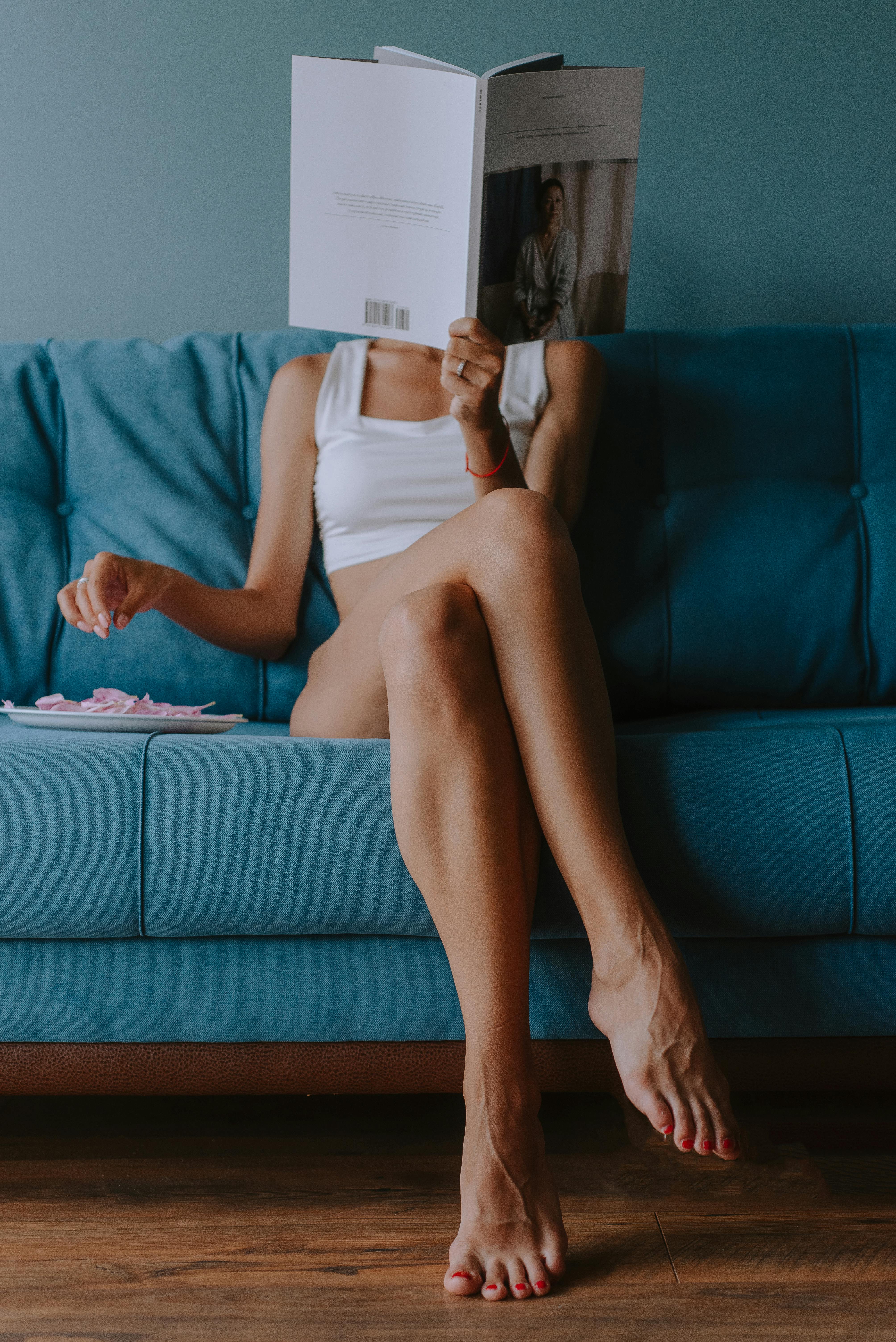 sexy woman sitting on blue sofa reading a magazine