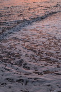 Waves gently wash the beach under a serene sunset sky, capturing the essence of tranquility.
