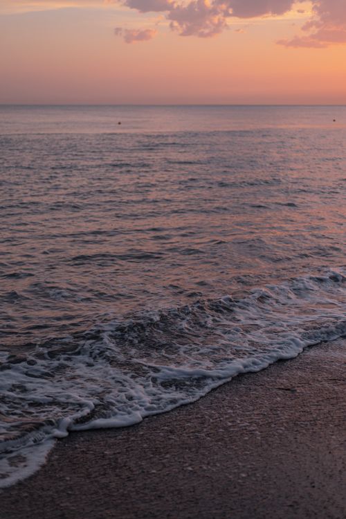 Free A peaceful sunset casting a warm glow over the ocean with gentle waves lapping the shore. Stock Photo