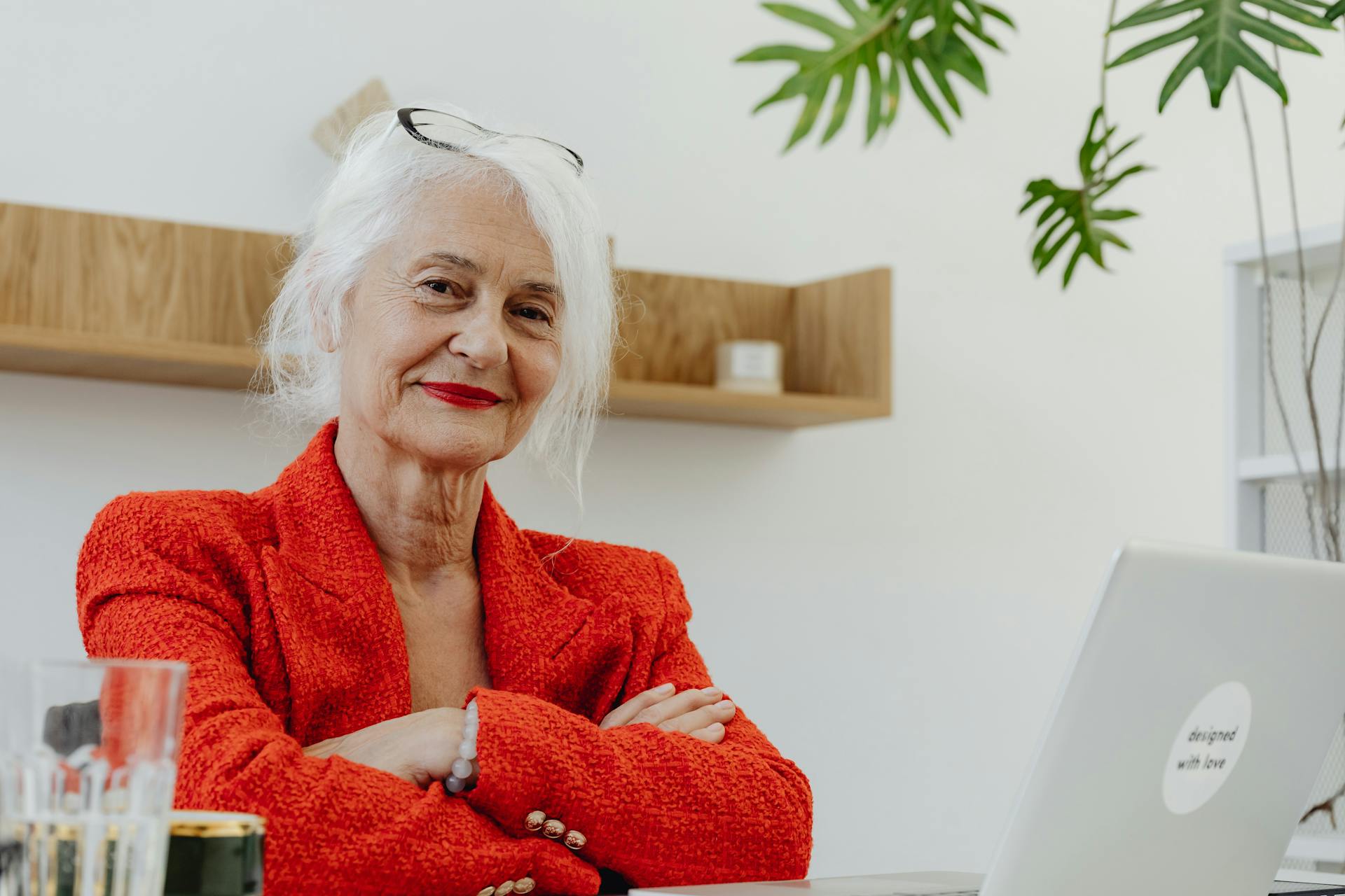 Elderly businesswoman with white hair smiling confidently at laptop in office setting.