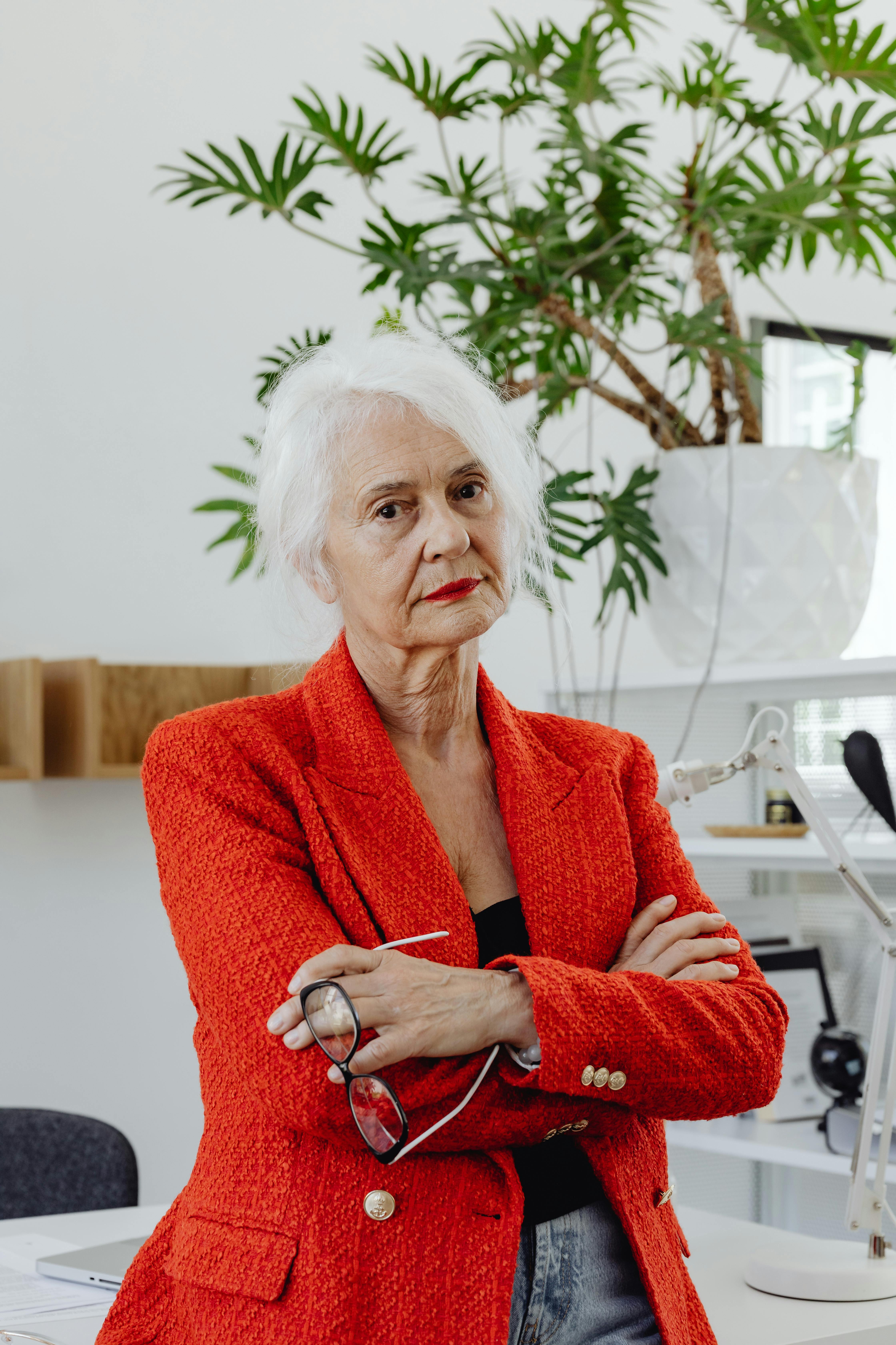 an elderly woman in knitted blazer holding an eyeglasses with her arms crossed