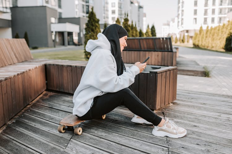 Woman Sitting On A Skateboard Using A Smartphone