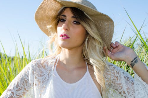 Free Woman Wearing Brown Hat and White Cardigan Standing in Middle of Grass Field Stock Photo