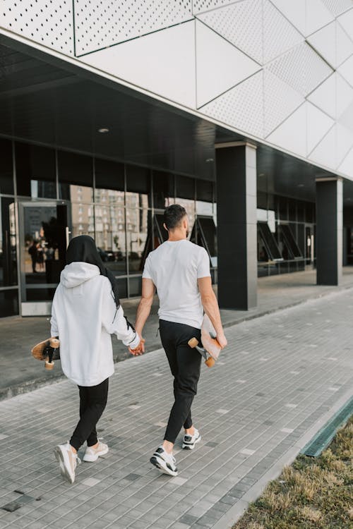 A Couple Holding Skateboards Holding Hands While Walking