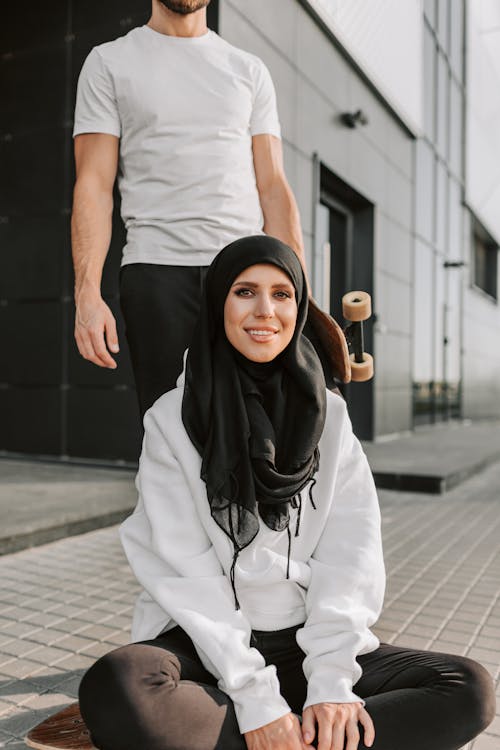 A Woman in Black Hijab and White Sweater Sitting on the Street