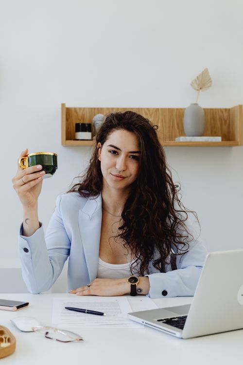 Free Professional woman in business attire holding a coffee cup in a modern office setting. Stock Photo