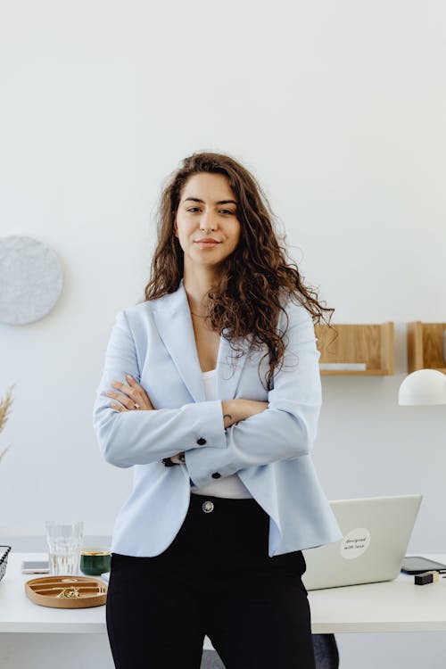 Free A Woman in White Blazer Smiling with Her Arms Crossed Stock Photo
