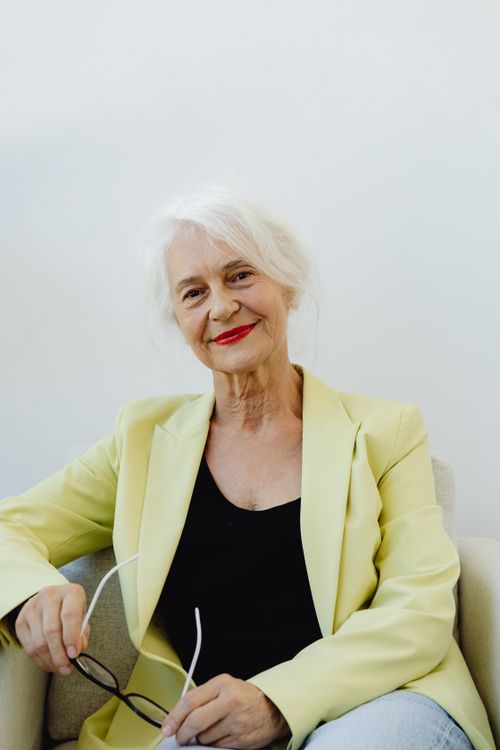 Free Elegant senior woman smiling in a yellow blazer, sitting on a chair. Stock Photo
