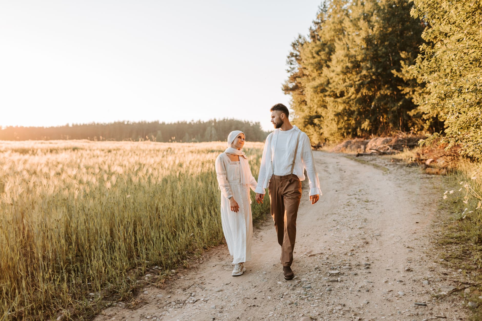 A couple in love walking hand in hand along a scenic dirt road at sunset.