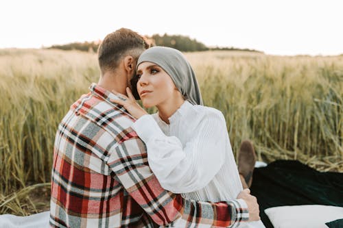 Free A Couple Embracing Each Other while Sitting on the Field Stock Photo