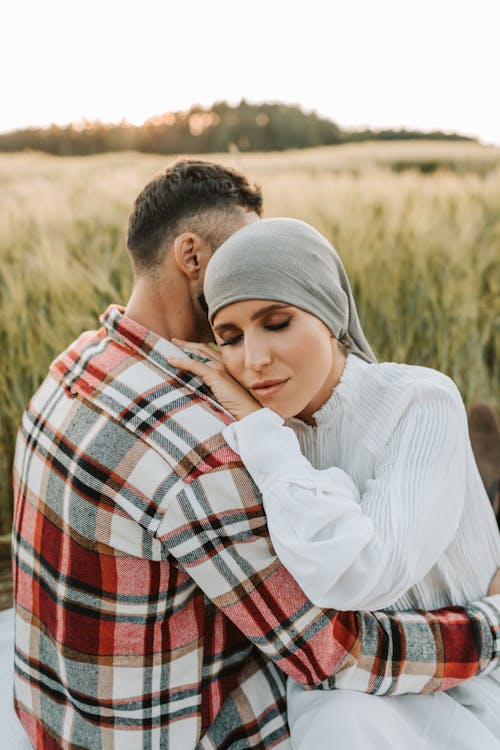 Free A Woman in White Long Sleeves Hugging a Man in Plaid Long Sleeves with Her Eyes Closed Stock Photo