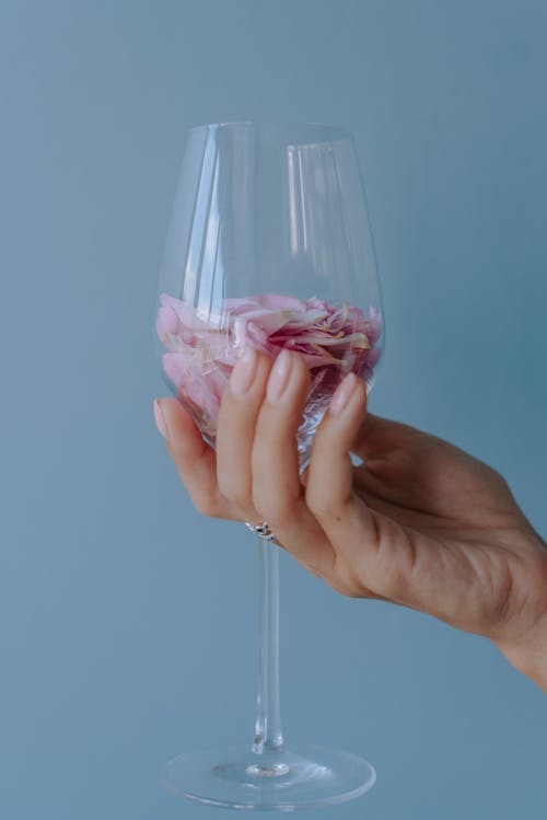 Free A Person Holding a Wine Glass with Pink Rose Petals Stock Photo