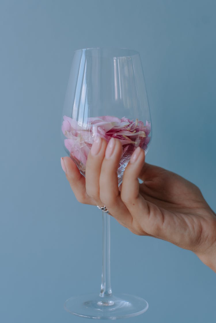 A Person Holding A Wine Glass With Pink Rose Petals