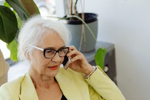 Free Elderly woman with white hair and eyeglasses using cellphone indoors. Stock Photo