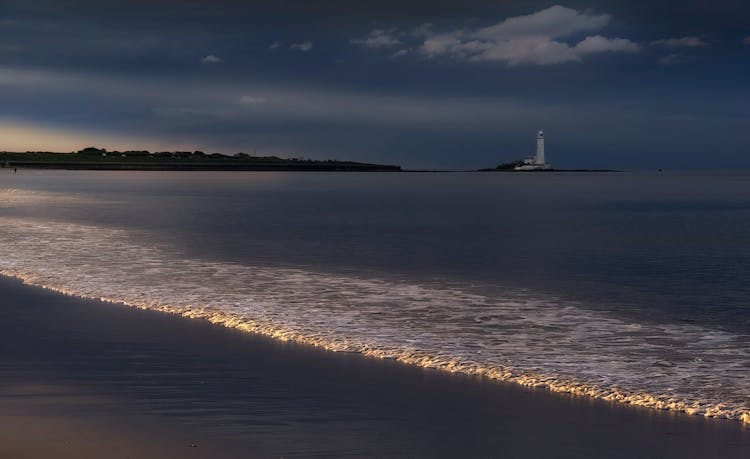 Seascape At Dusk With Wave And Lighthouse On A Horizon