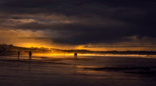 Free Capture the dramatic allure of a beach during sunset with silhouetted figures against a glowing sky. Stock Photo