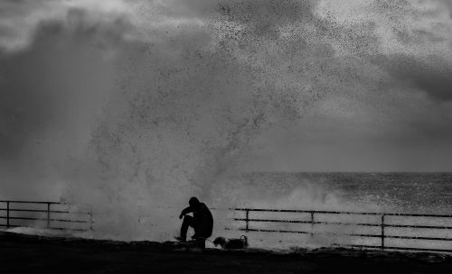 Free Dramatic silhouette of a man near crashing ocean waves against railings. Stock Photo