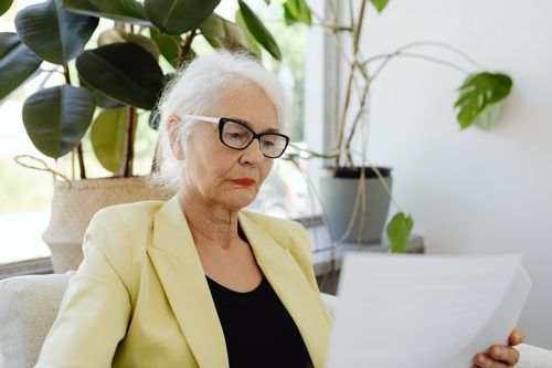 Free Confident senior woman in yellow jacket reading documents indoors. Stock Photo