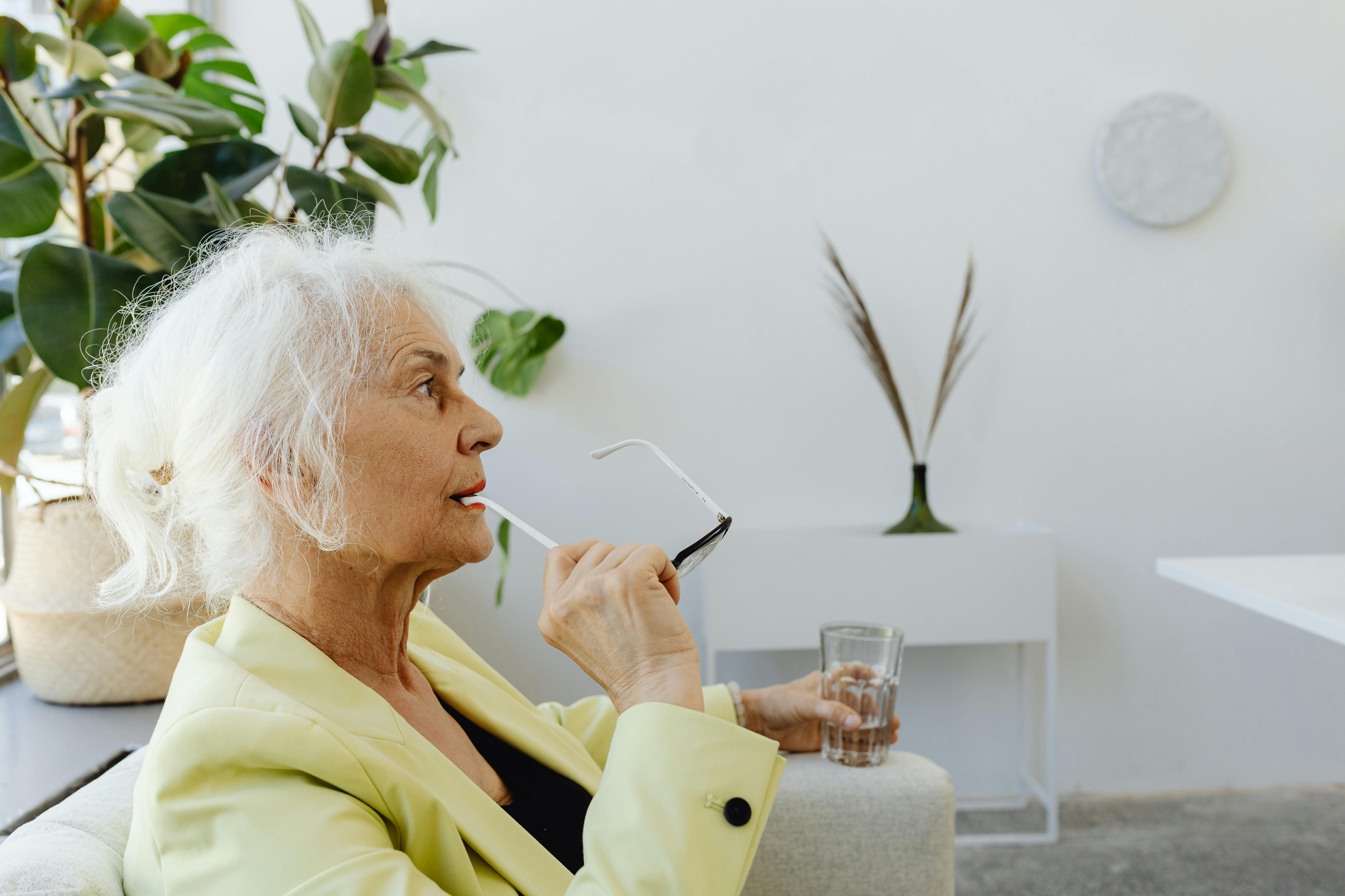Senior woman in a stylish indoor setting, wearing glasses and a green blazer.
