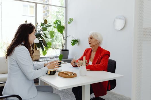 Businesswomen engaged in a professional discussion at an office desk with plants.