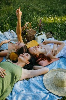 Three women enjoying a sunny day picnic in the park, relaxing on a blue blanket.