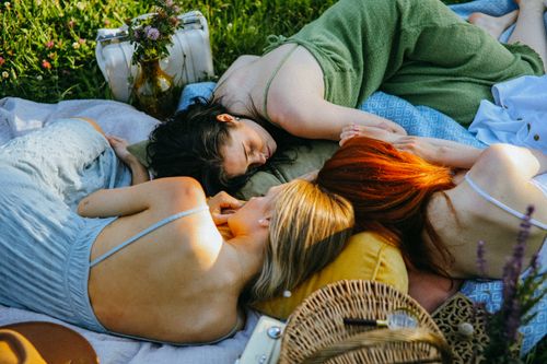 Free Three adults enjoy a tranquil picnic on a sunny day, lying on a blanket in a meadow. Stock Photo