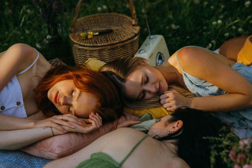 Free Three women resting outdoors on a cozy picnic setup, enjoying a peaceful nap in a grassy area. Stock Photo