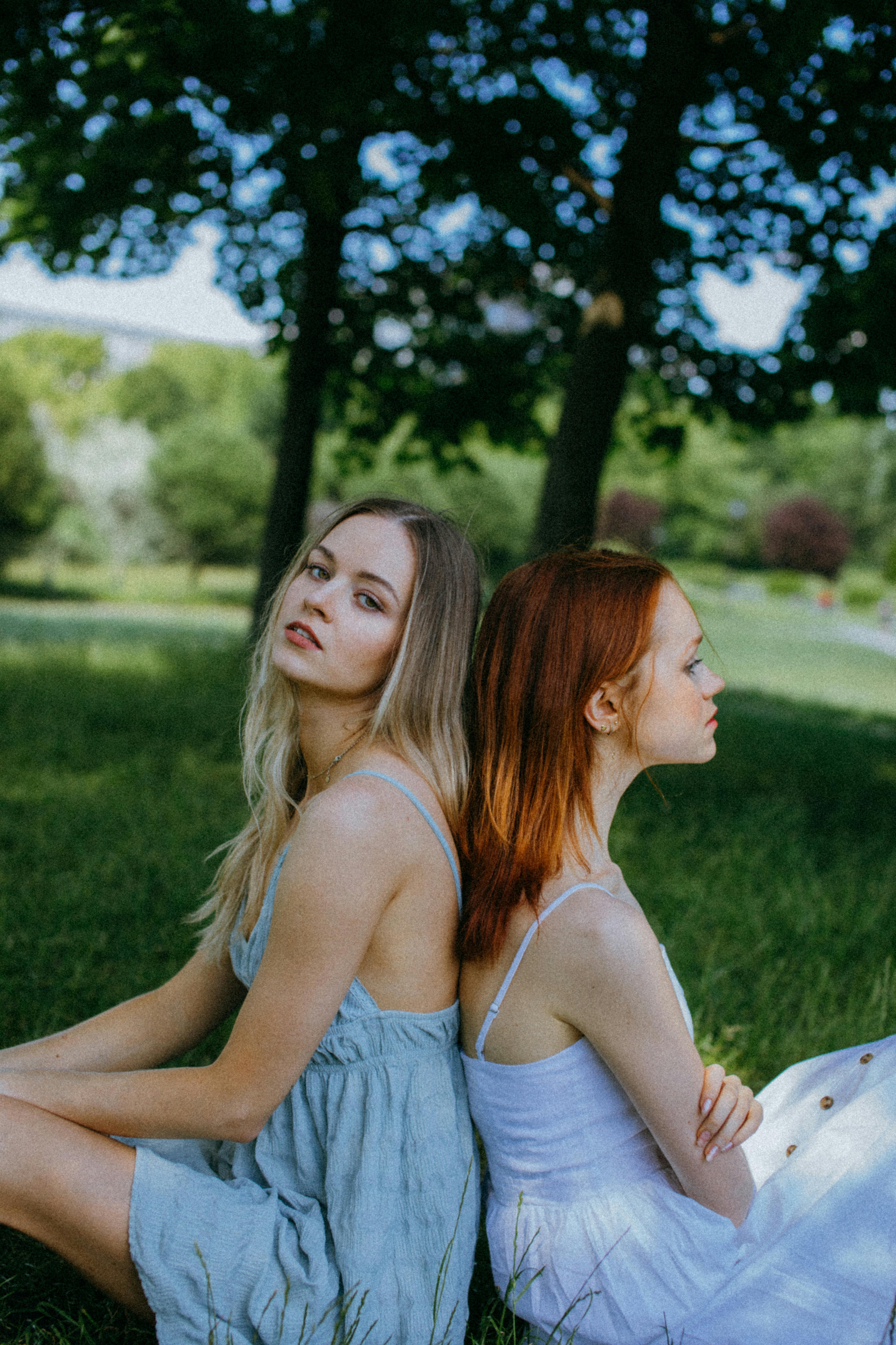 women sitting back to back on green grass