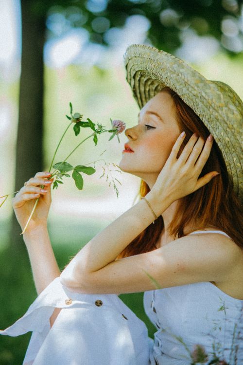 Free A woman in a straw hat enjoys the aroma of a flower on a sunny summer day. Stock Photo