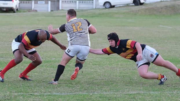 Three rugby players in action during outdoor game on a grassy field.