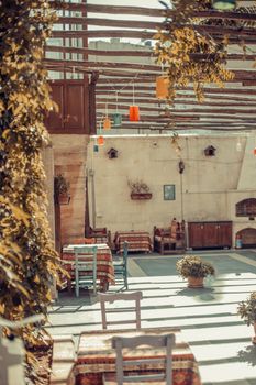 A cozy outdoor restaurant patio featuring rustic tables, chairs, and colorful lanterns under a wooden pergola.