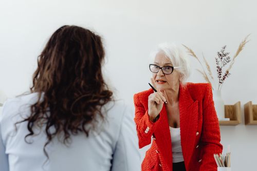 Free Senior woman in red jacket leading an authoritative discussion in an office setting. Stock Photo