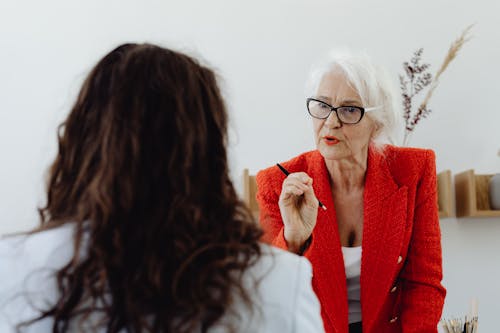 An Elderly Woman in Red Blazer Talking to the Person with Curly Hair