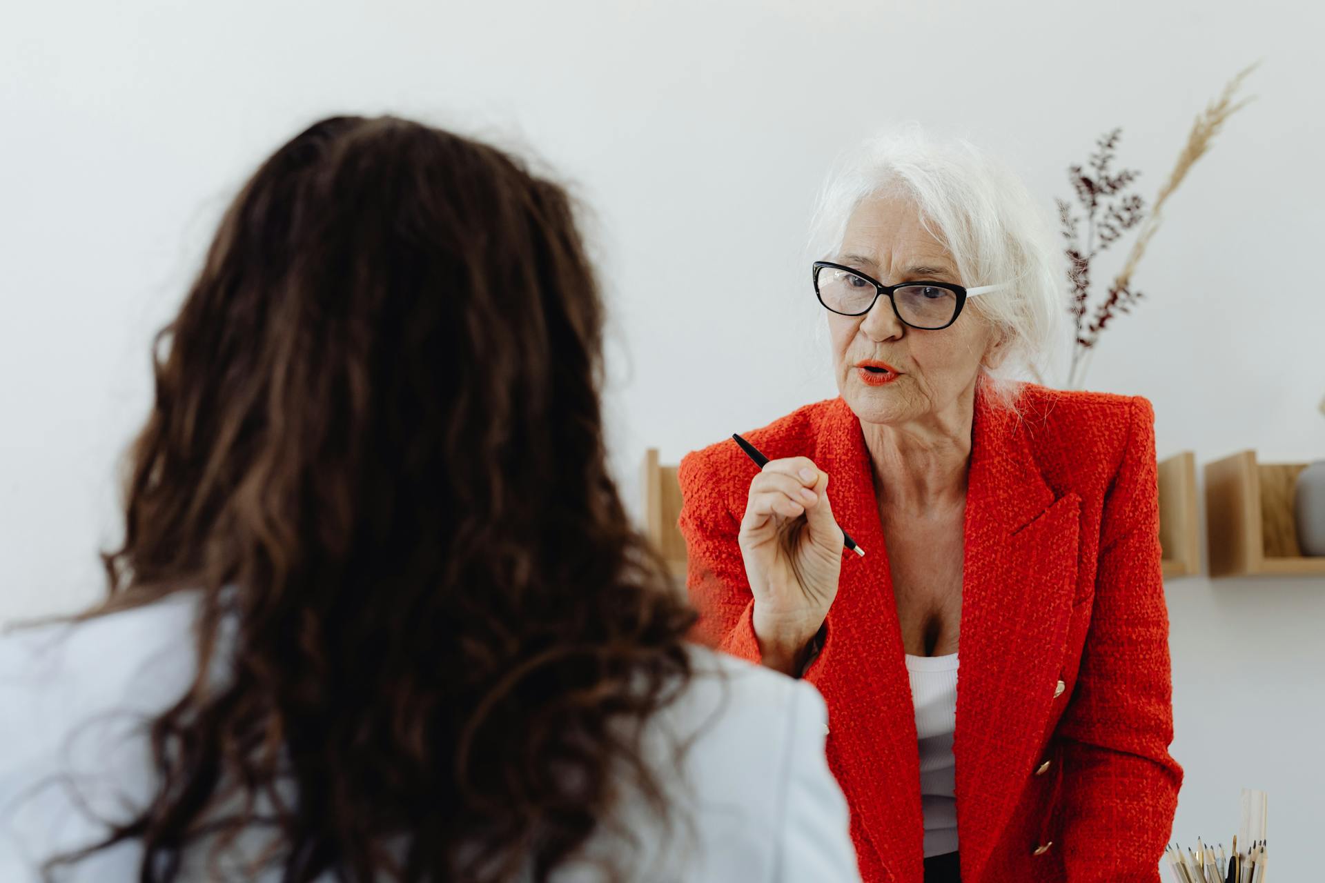 Confident senior businesswoman in red blazer discussing with a colleague in an office setting.