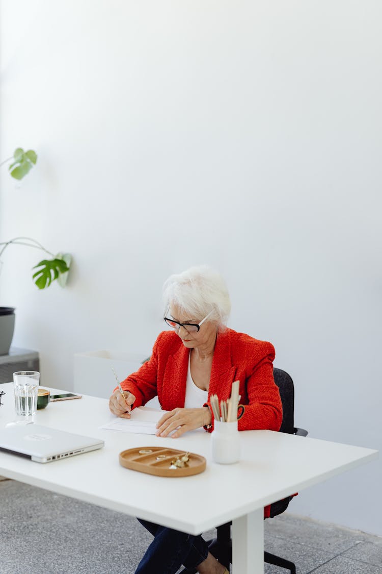 A Woman In Red Jacket Sitting At A White Desk