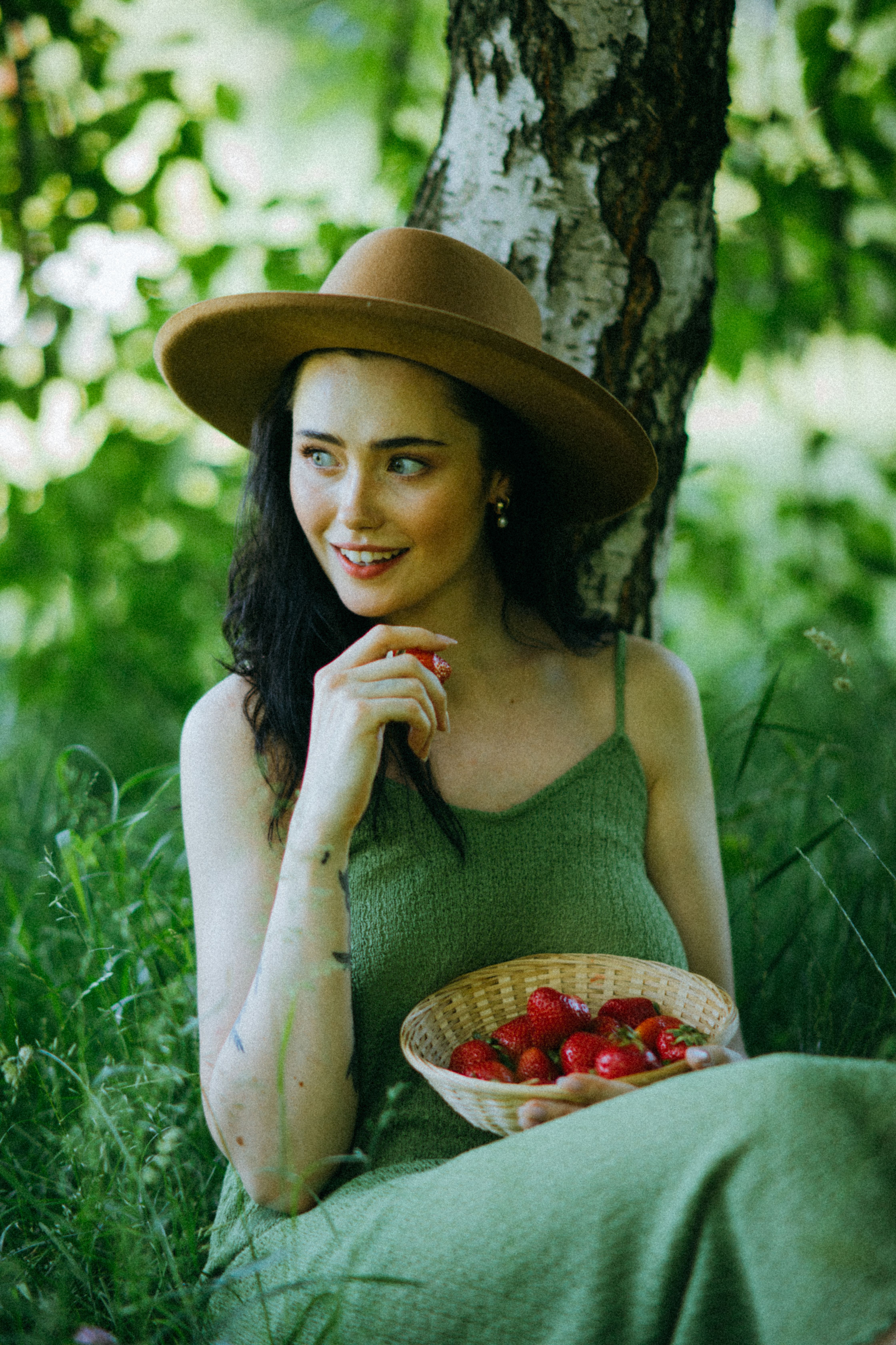 A woman in a green dress relaxes outdoors with fresh strawberries, exuding a sense of joy and tranquility.