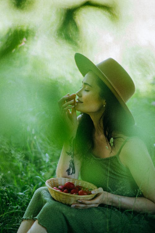 Woman Wearing Hat Smelling a Strawberry