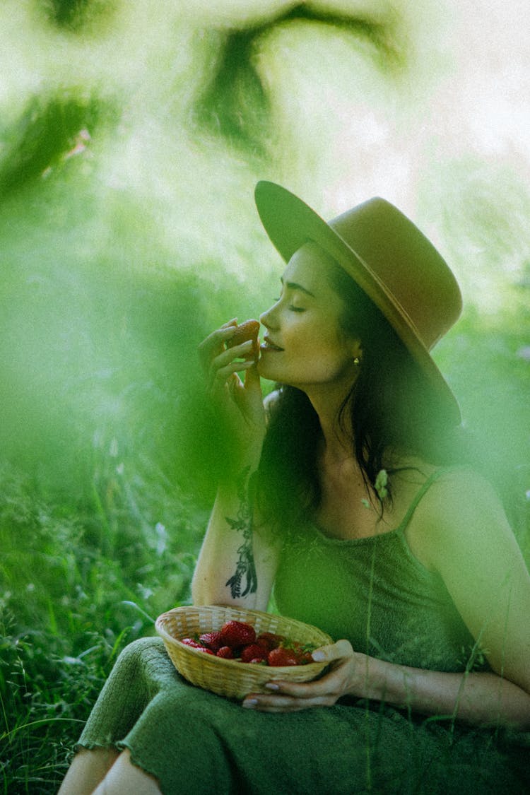 Woman Wearing Hat Smelling A Strawberry