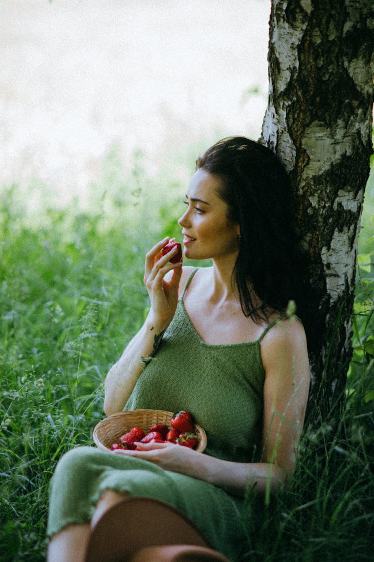 
A Woman Eating Strawberries While Leaning On A Tree