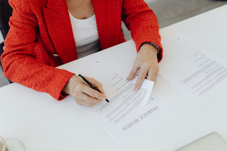 A Woman In Red Blazer Signing A Paper 