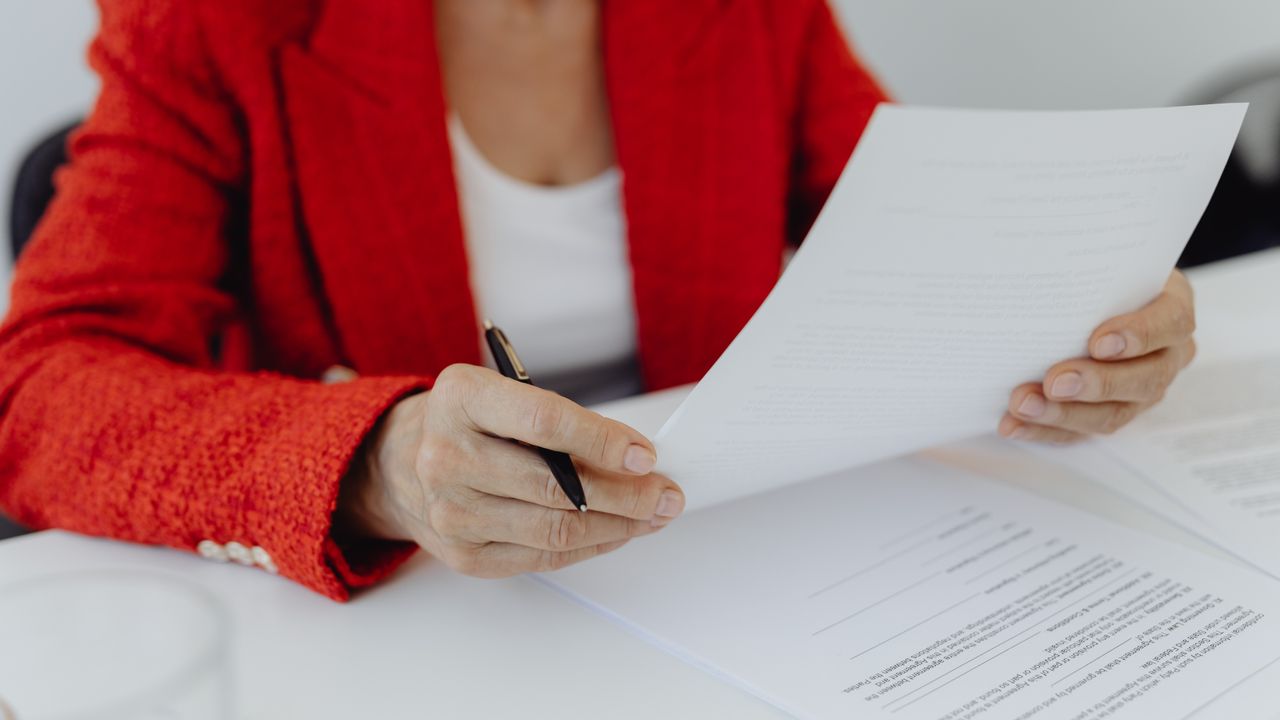Close-up of a person in a red jacket reviewing documents with a pen in hand.