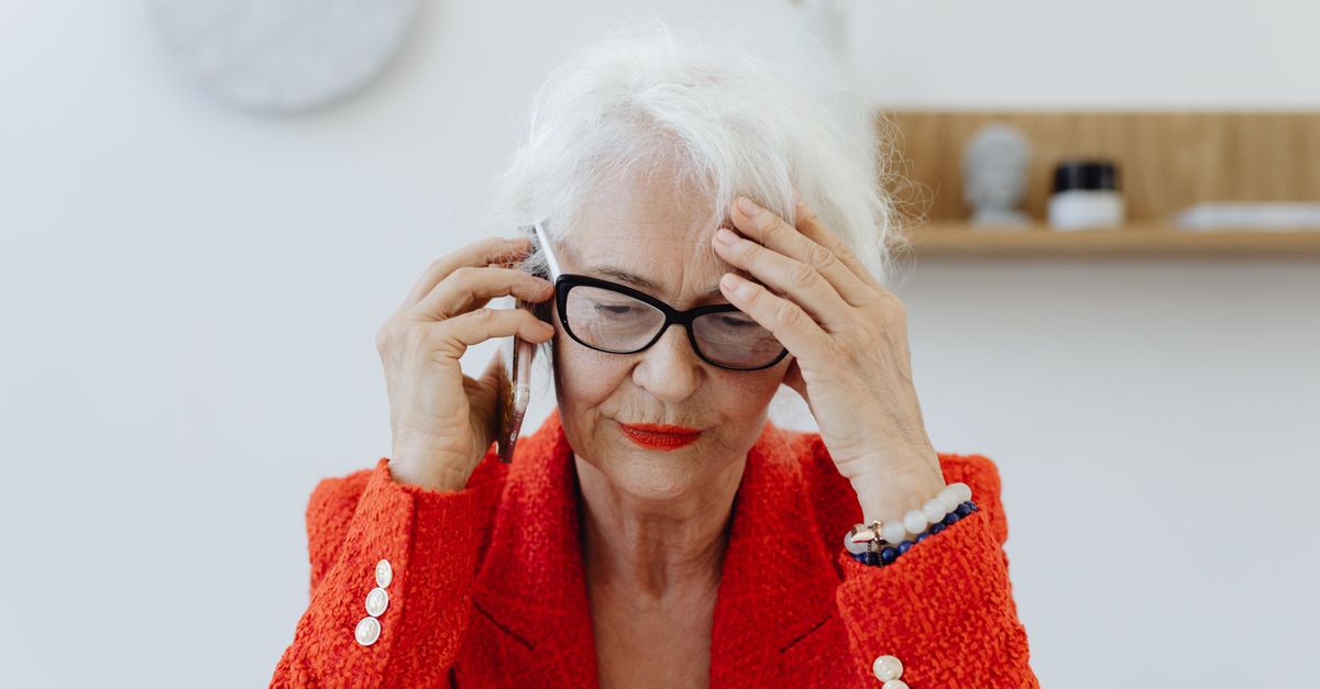 A person in a red blazer concentrating on a phone call indoors